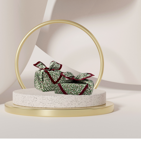 A luxury reusable fabric gift wrap with a holly pattern, featuring red berries and green leaves on a white background, eco friendly, personalised through embroidery 