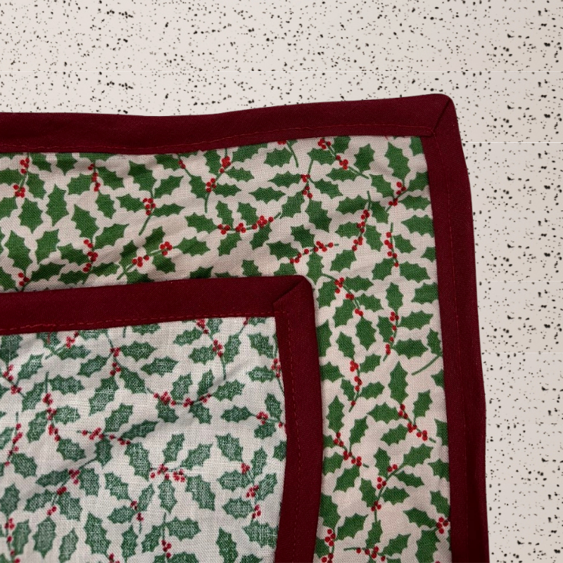 A luxury reusable fabric gift wrap with a holly pattern, featuring red berries and green leaves on a white background, eco friendly, personalised through embroidery 