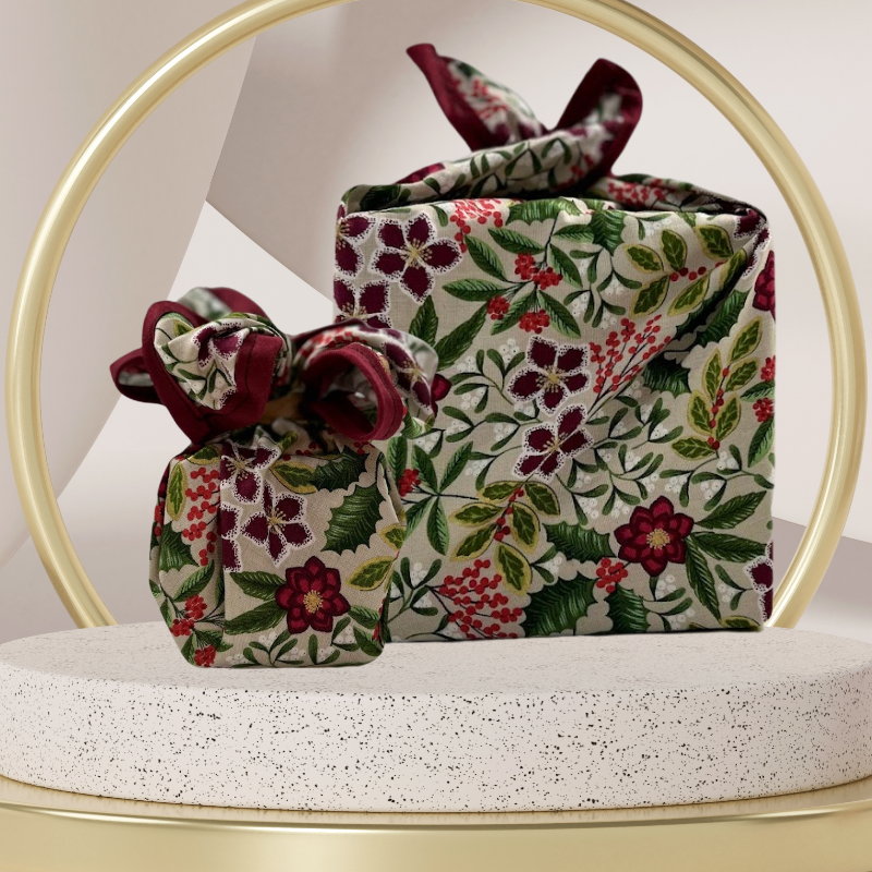 A fabric gift wrap with a festive floral design featuring crimson leaves and glistening berries against a grey background. Luxury, eco-friendly, embroidery personalisation  
