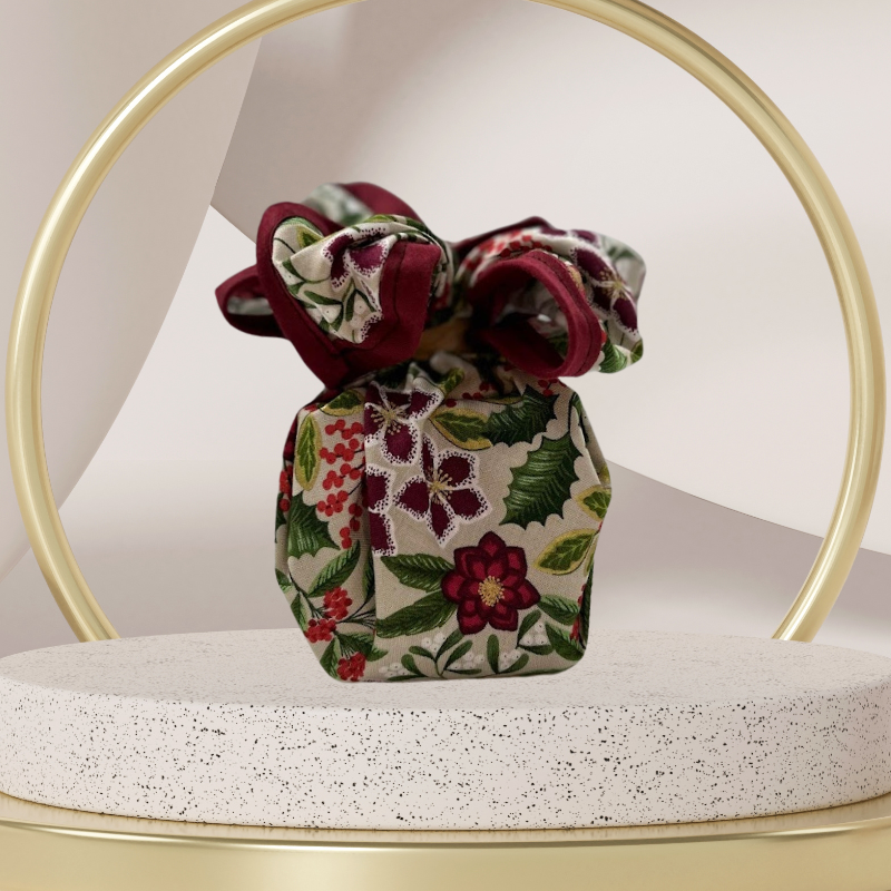 A fabric gift wrap with a festive floral design featuring crimson leaves and glistening berries against a grey background. Luxury, eco-friendly, embroidery personalisation  