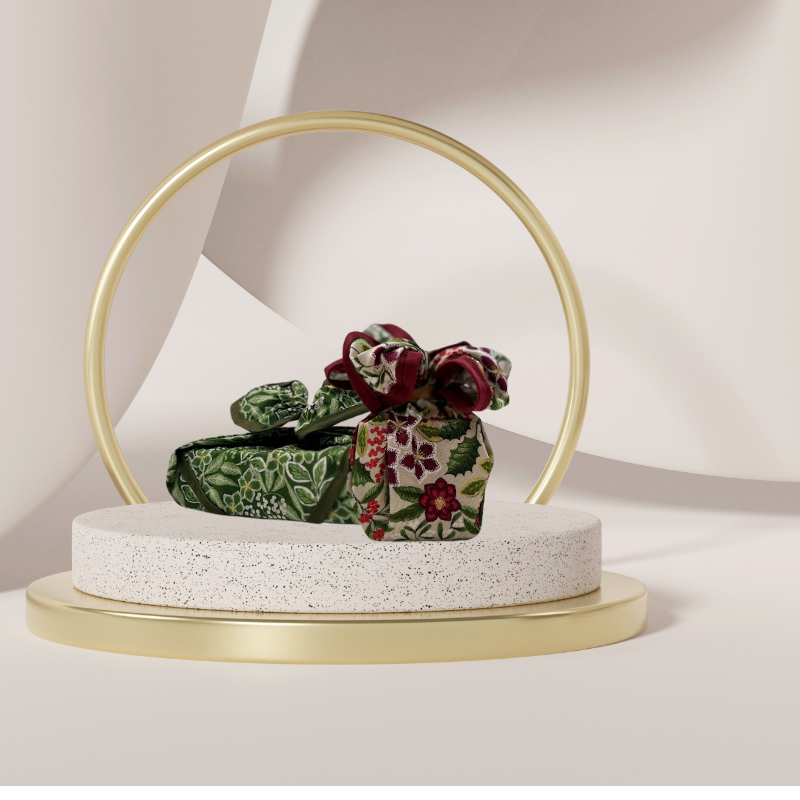 A fabric gift wrap with a festive floral design featuring crimson leaves and glistening berries against a grey background. Luxury, eco-friendly, embroidery personalisation  