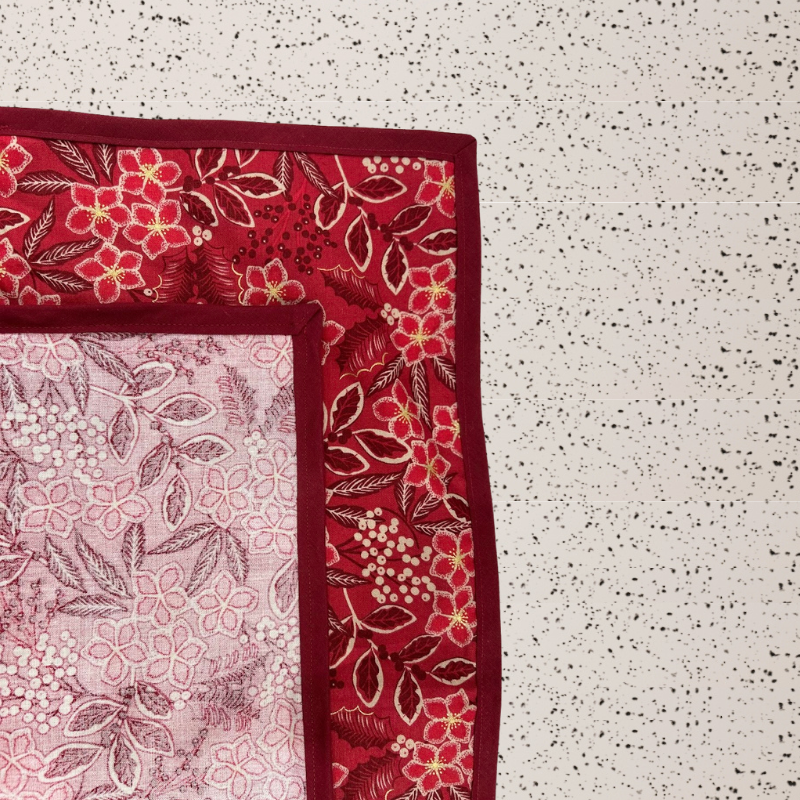 A fabric gift wrap with a Christmas-themed floral pattern, featuring red and green colours and gold accents. Luxury, eco-friendly, embroidery personalisation   