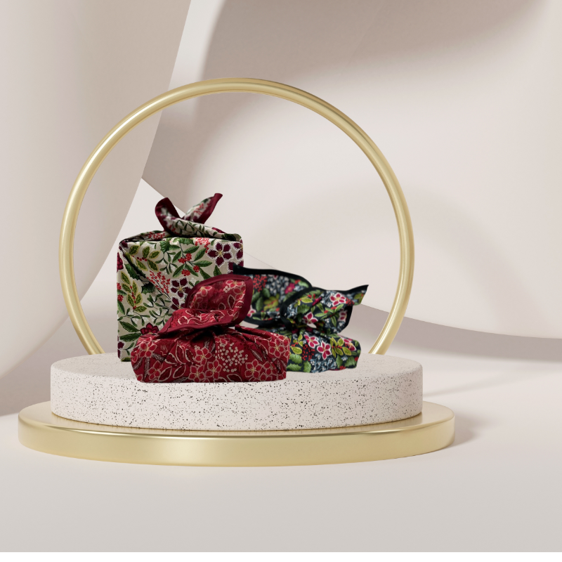 A fabric gift wrap with a Christmas-themed floral pattern, featuring red and green colours and gold accents. Luxury, eco-friendly, embroidery personalisation   