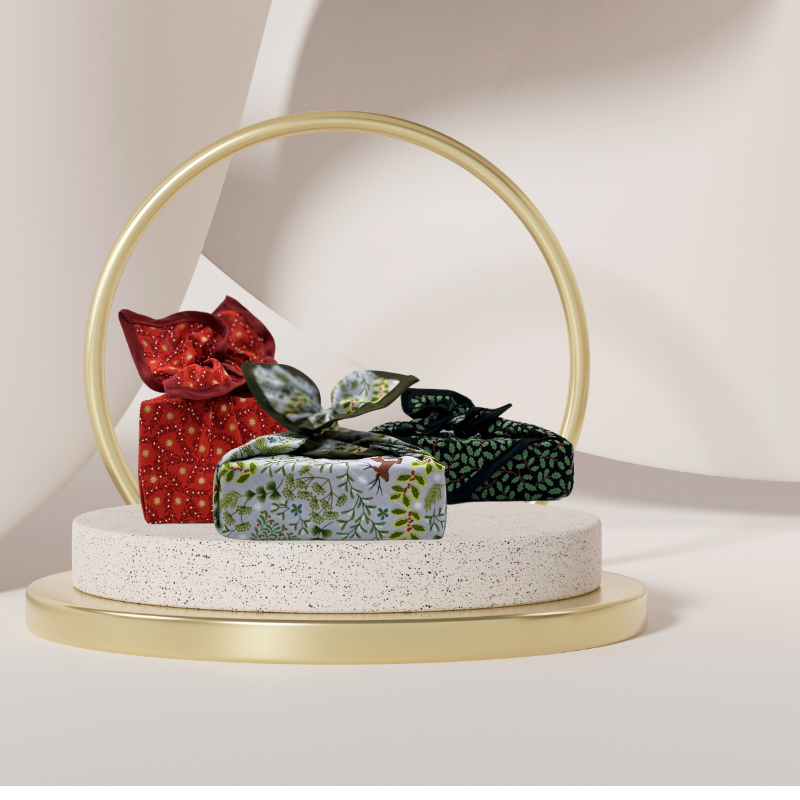 A reusable fabric gift wrap with a Christmas-themed design featuring reindeer, snowflakes, evergreen trees, and floral detail.
Luxury, eco-friendly, embroidery personalisation 
Next to red and green tranditional 