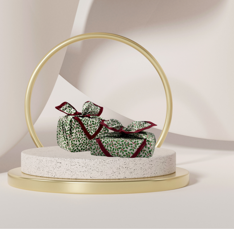 A luxury reusable fabric gift wrap with a holly pattern, featuring red berries and green leaves on a white background, eco friendly, personalised through embroidery 